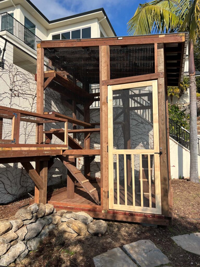 A spacious custom-built outdoor cat enclosure or catio made of wood and wire mesh situated against a modern home in San Rafael California featuring multiple levels ramps and a secure entrance for easy access.